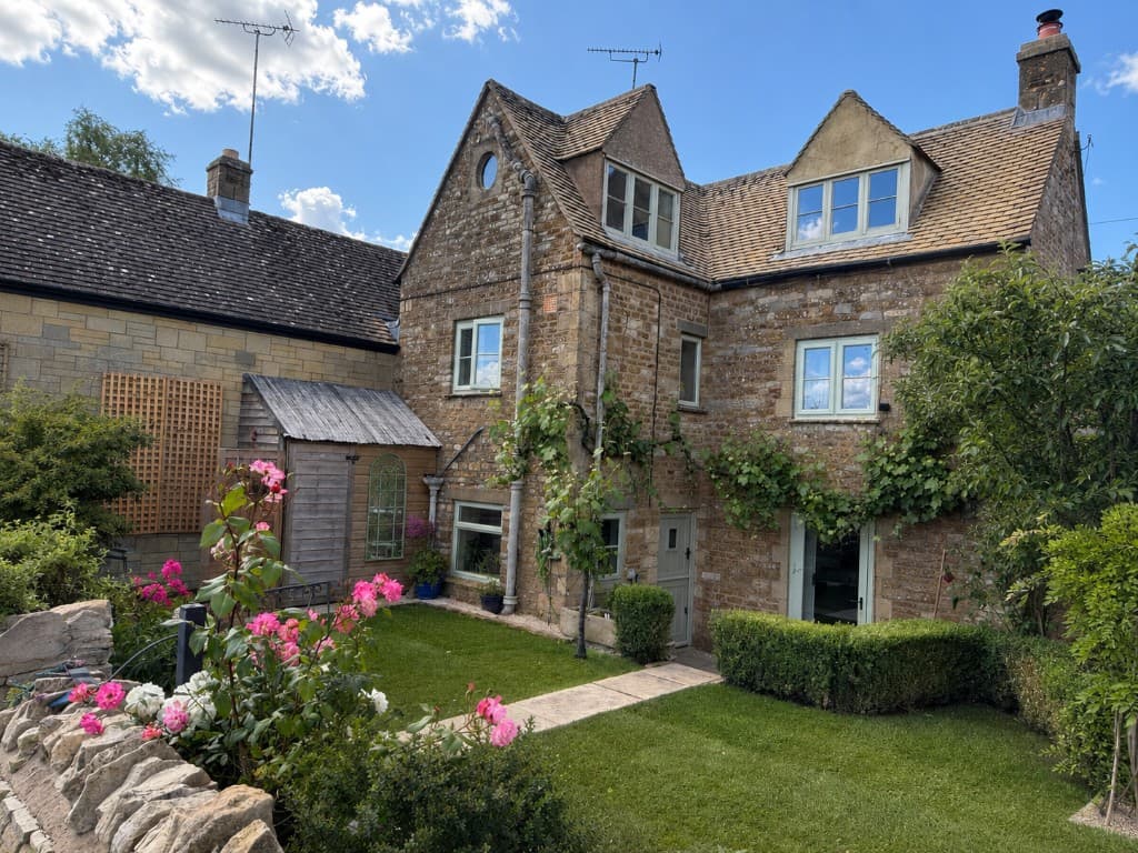 Honey-stone cottage front with climbing roses and green lawn